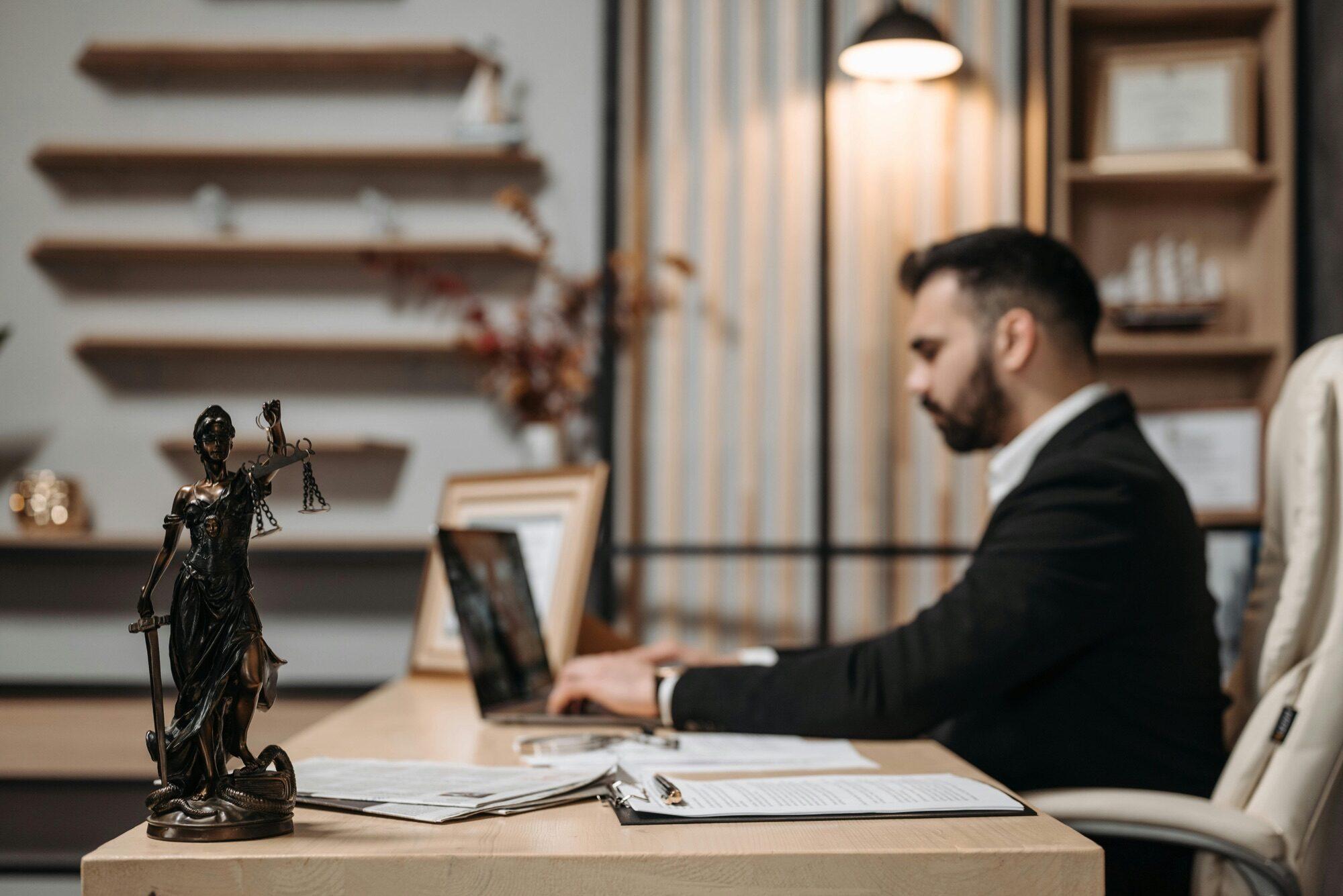 Attorney working at a laptop with a Lady Justice statuette on the desk
